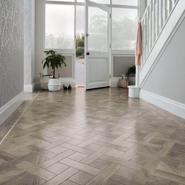 A white front door is bordered by Karndean wooden block style flooring in neutral tones