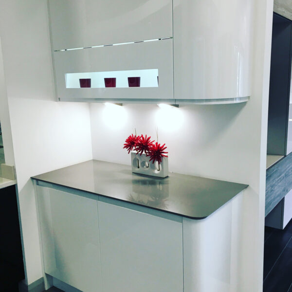 High Gloss White Curved Cabinet Corner with Undercabinet Lighting Above and Below, Metallic Gloss Curved Cabinet, Dark-Toned Worktops Designed by Cavendish Kitchens