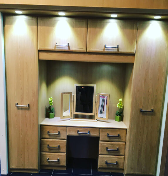 Wooden Built-In Wardrobe in Bedroom with Integrated Dresser Section Below, Triple Mirror, Under Cabinet Lighting for Vanity Area, and Ceiling-Integrated LED Lights