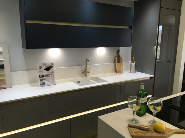 Modern handleless kitchen cabinets in gold and navy housing a sink with gold tap and white worktop