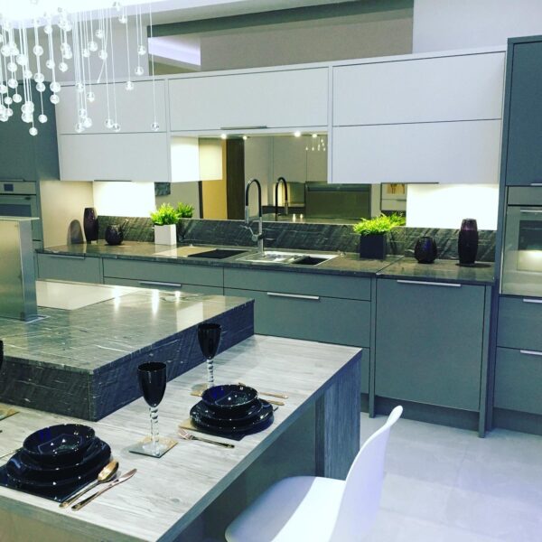 Double-Layered Mint Green Pull-Out Cabinet Drawers Overhead, Mirrored Splashback Next to Silver Kitchen Sink, Dark Green Lower Level Cabinets and Drawers, Integrated Double Oven, Under Cabinet Lighting, Island Table with Seating Around