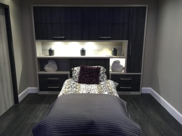 Bespoke built-in wardrobes in dark grey with integrated lighting surround a single bed