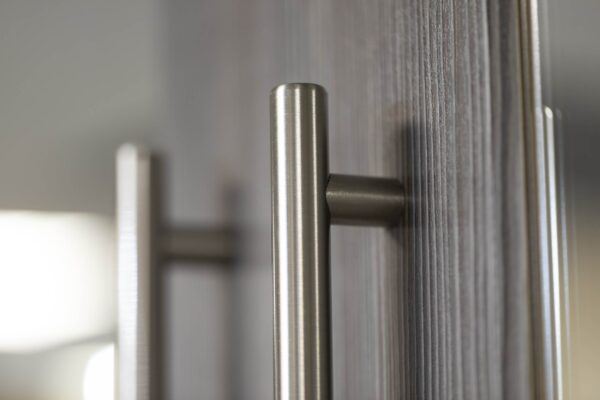 Close-up shot of a shiny silver cabinet handle and a dark wood-style cabinet door