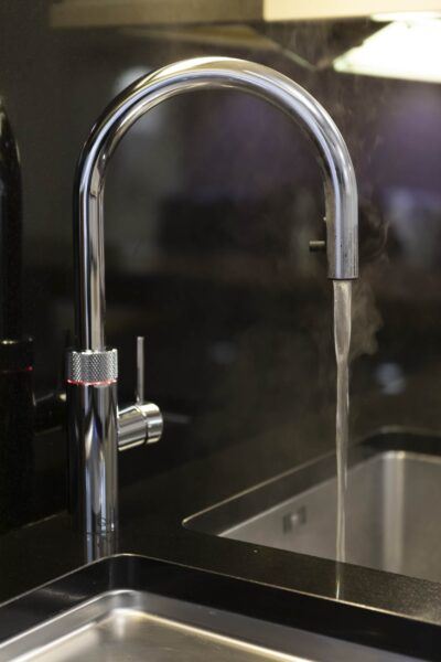 Close-up of a boiling hot water tap with a red light on, contrasting against a black kitchen splashback and dark marble kitchen worksurfaces