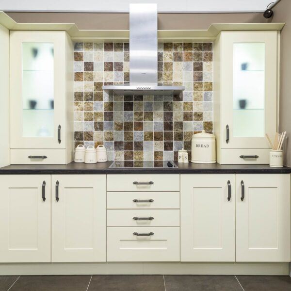 Captivating white kitchen complemented by black worktop, cream cabinets, tiled splashback, extractor fan, and electric hob