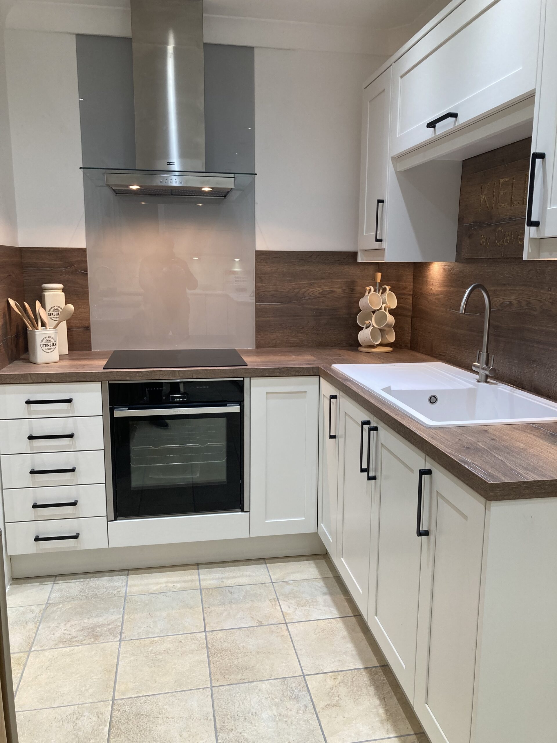 Cavendish kitchen featuring white painted shaker cabinet doors, wooden surfaces, a wood splashback, tiled floor, and an integrated sink.
