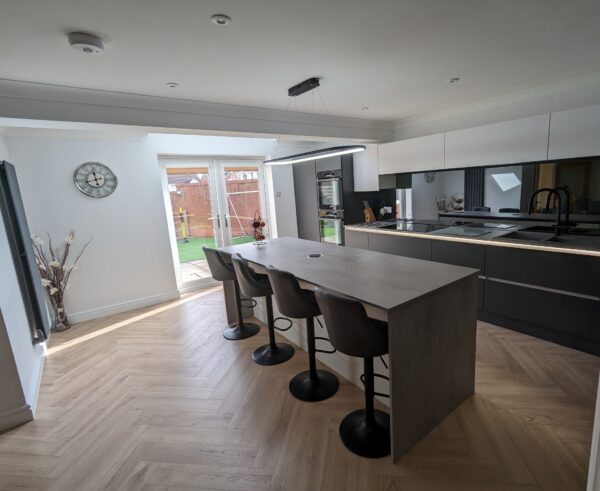 Cavendish-designed kitchen with Veneto Graphite Matt and Veneto White Matt cabinet doors and a handleless rail system. The worktops are Chromix Silver Laminate, paired with warm wood-effect Karndean flooring. Plus, integrated double oven and pendant lighting over the island area